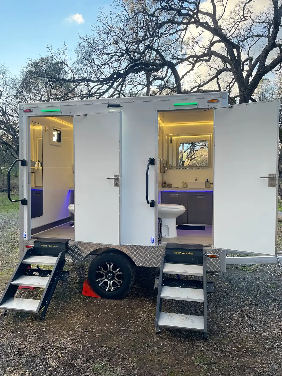 Two-door restroom trailer with lights on at an outdoor event