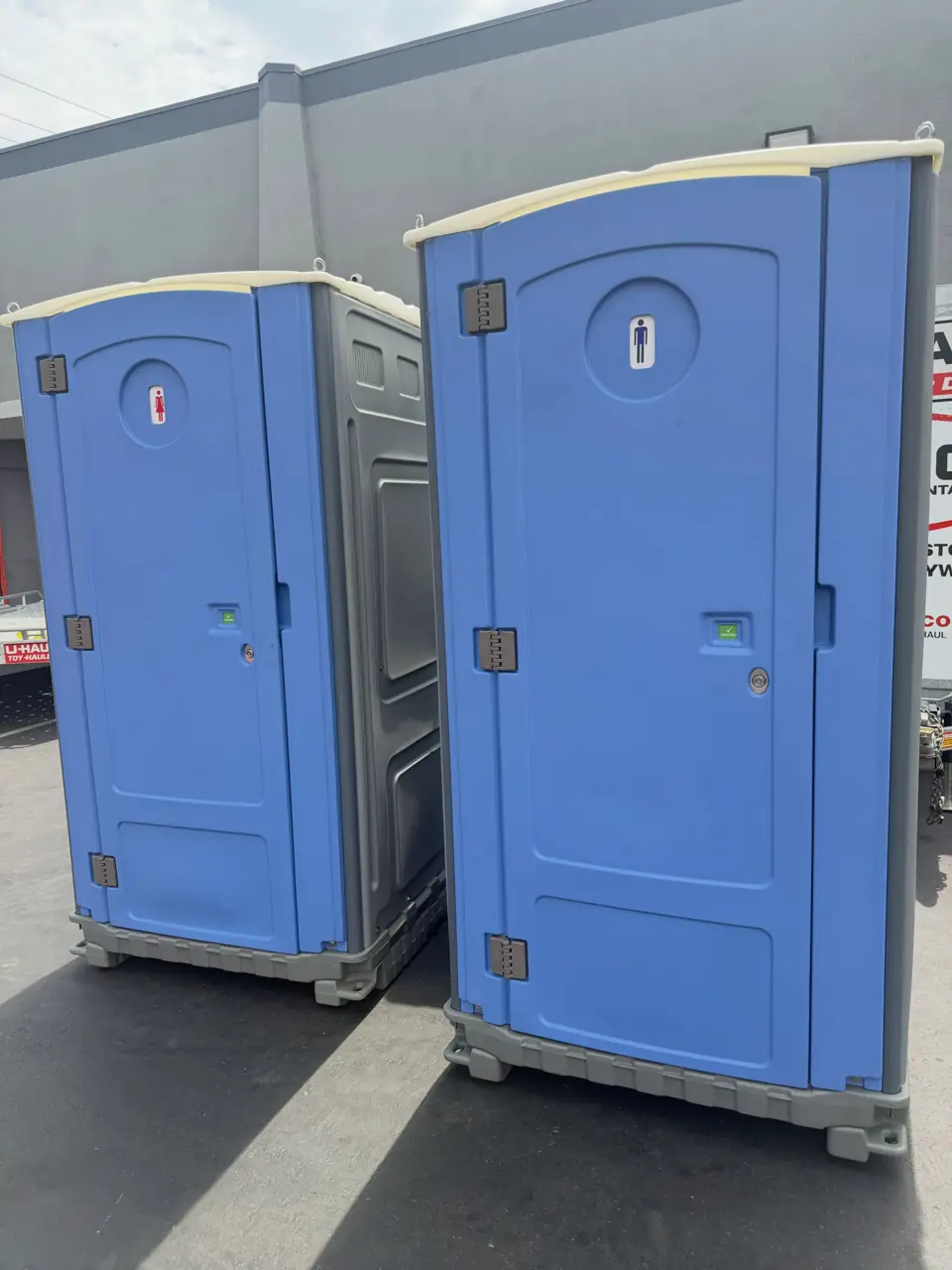 Two standard blue porta potties side by side on a paved lot